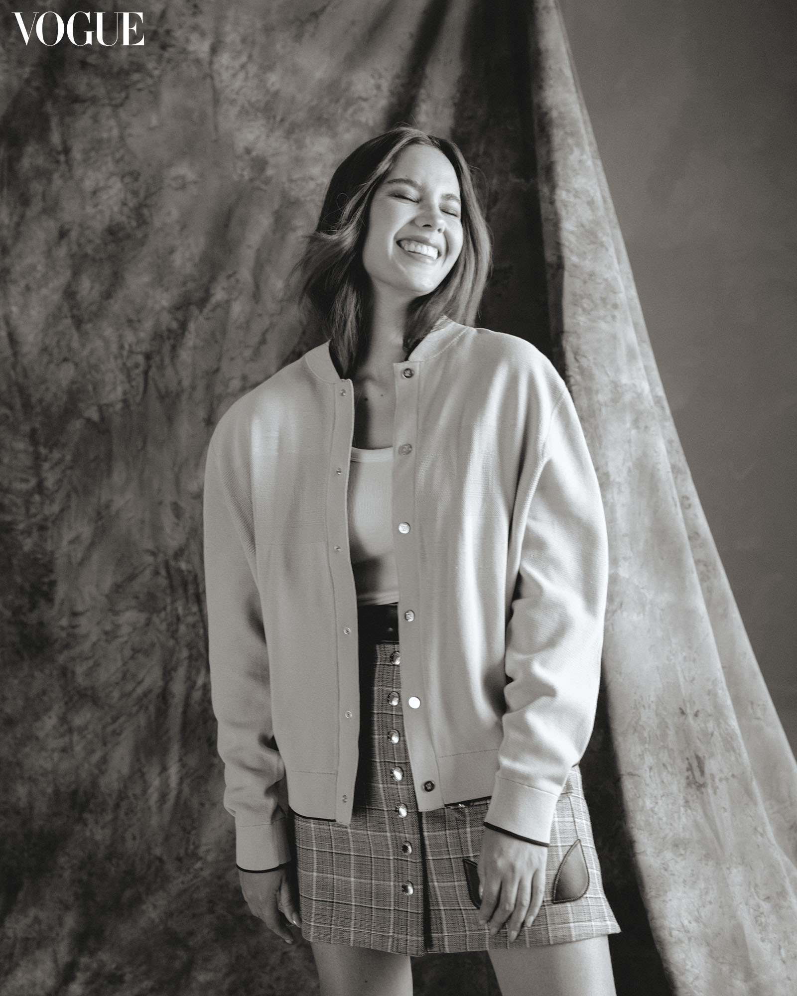 a black and white portrait of Catriona Gray smiling wearing a jacket and plaid skirt