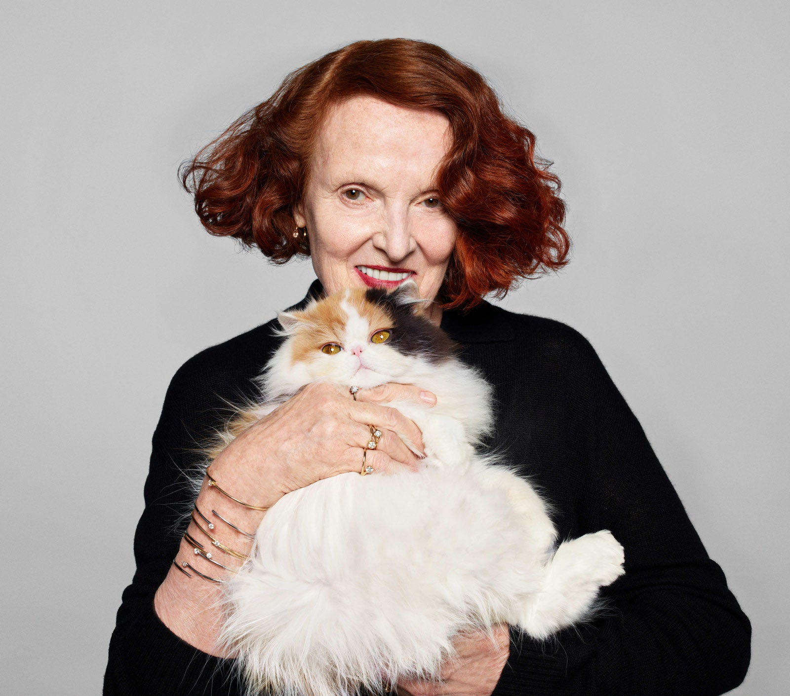 Portrait of an elder woman with red hair smiling and posing with her cat wearing pandora rings and bracelets as jewelry
