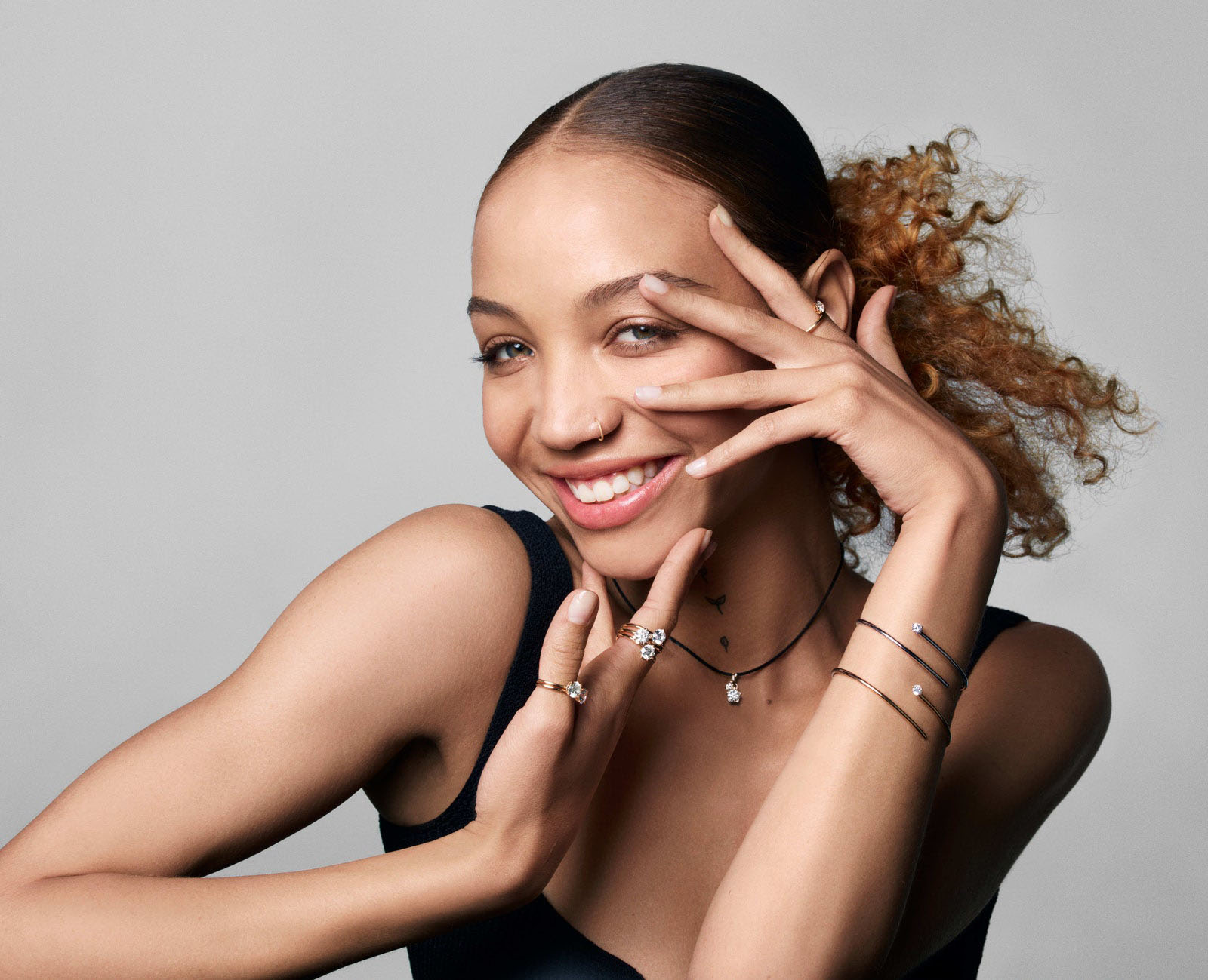 Portrait of a woman with slicked back curly brown hair smiling wearing pandora rings and bracelets as jewelry